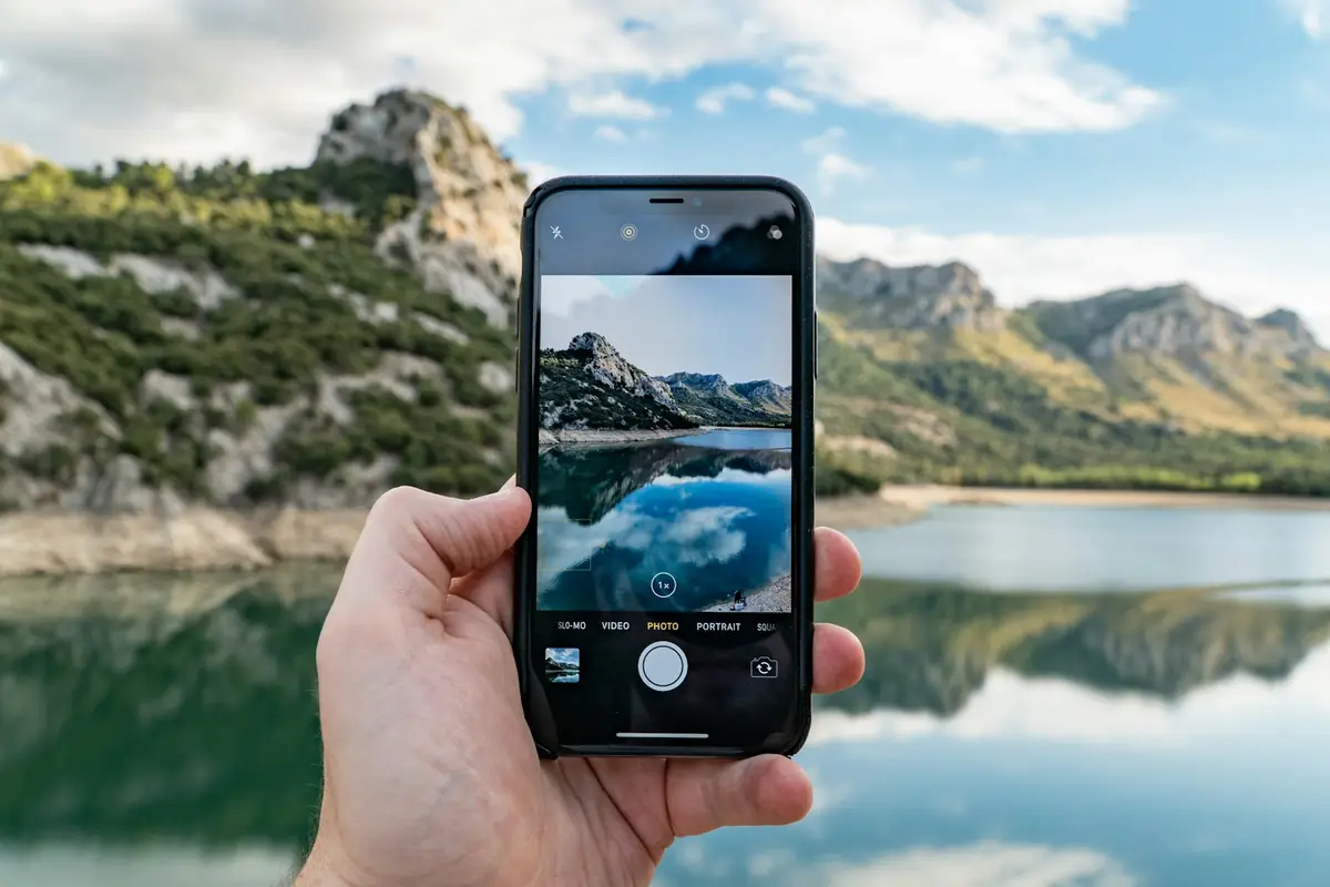 スマホのカメラで湖と山の景色を撮っている手元